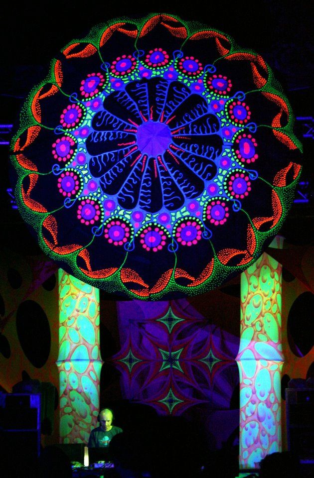 A vast ultraviolet mandala canopy in red, blue and green suspended above a DJ booth at night