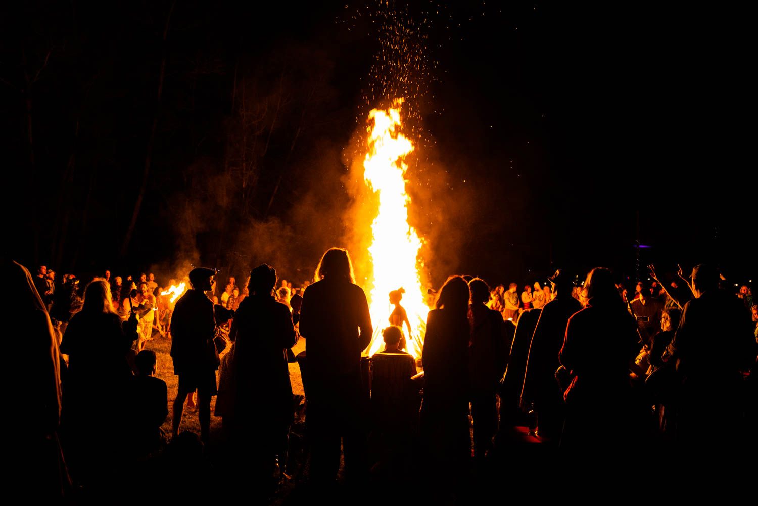 A crowd gathered in silhouette around a tall column of flame at night